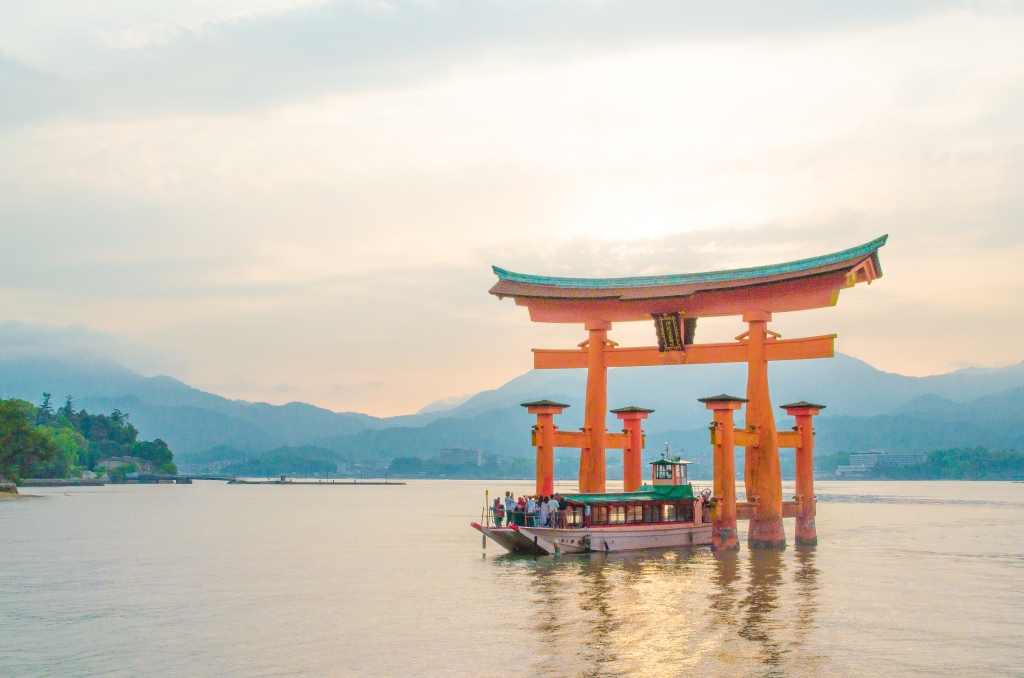 itsukushima shrine in miyajima during high tide with a boat sailing across it